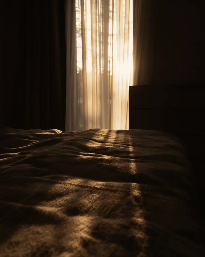 Low morning light through a curtain onto an empty bed.